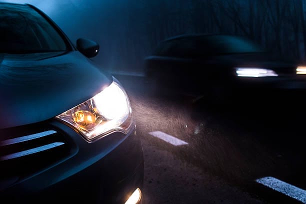Une voiture circulant sur la route la nuit avec ses phares allumés, assurant la visibilité des autres véhicules.
